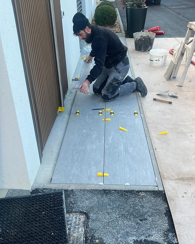 Un carreleur à genoux pose des carreaux devant une entrée d'immeuble