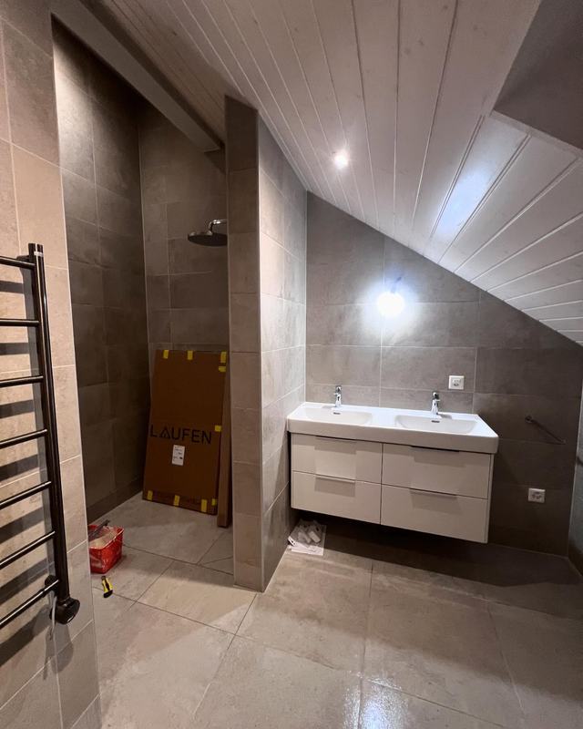 Salle de bain sous toit terminée : meuble vasque blanc, carrelage gris grand format, sèche-serviettes noir